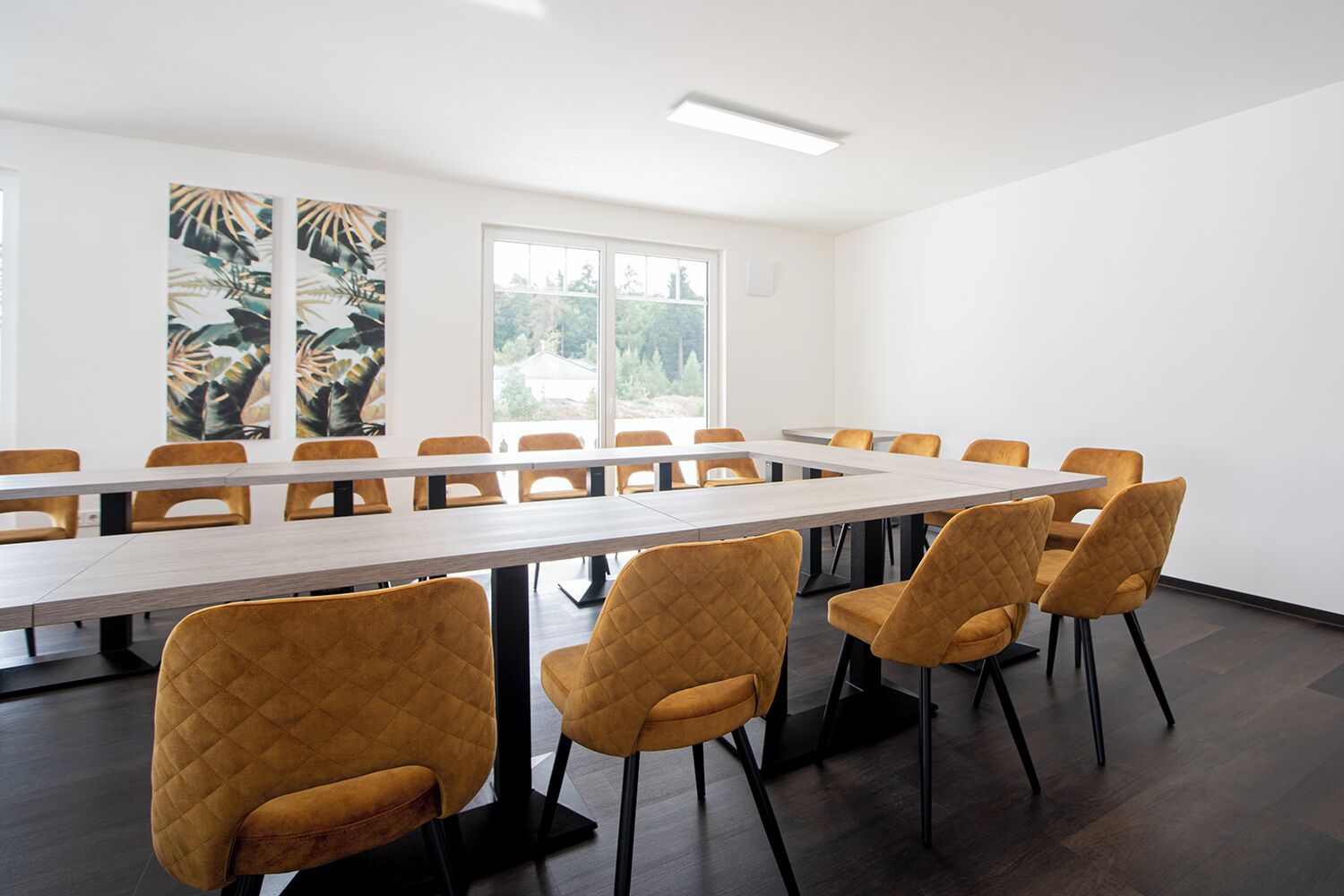 A conference room with a long table and several chairs, large windows, and tropical artwork on the walls.