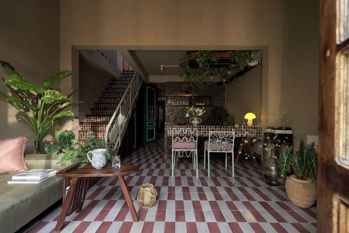 A cozy living room with a checkered floor, a sofa with a book, a coffee table, and a staircase leading to a balcony.