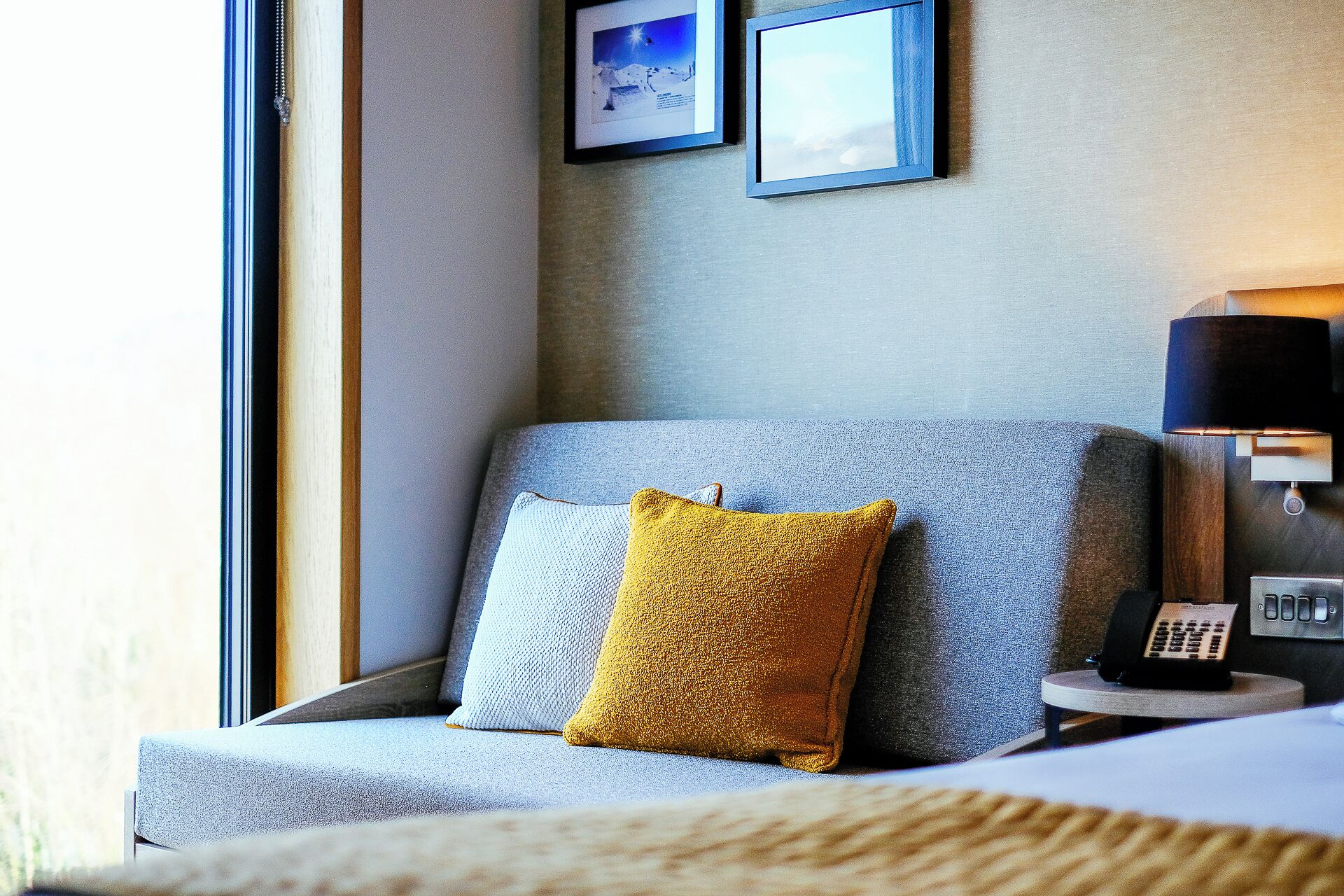 A modern hotel room with a grey sofa, a mustard-colored pillow, and a small table with a telephone.