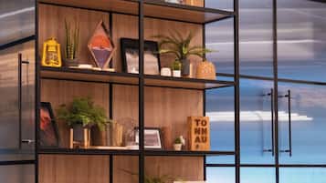 Un soggiorno moderno con un'ampia libreria piena di libri, oggetti decorativi e piante. In primo piano, un divano blu.
