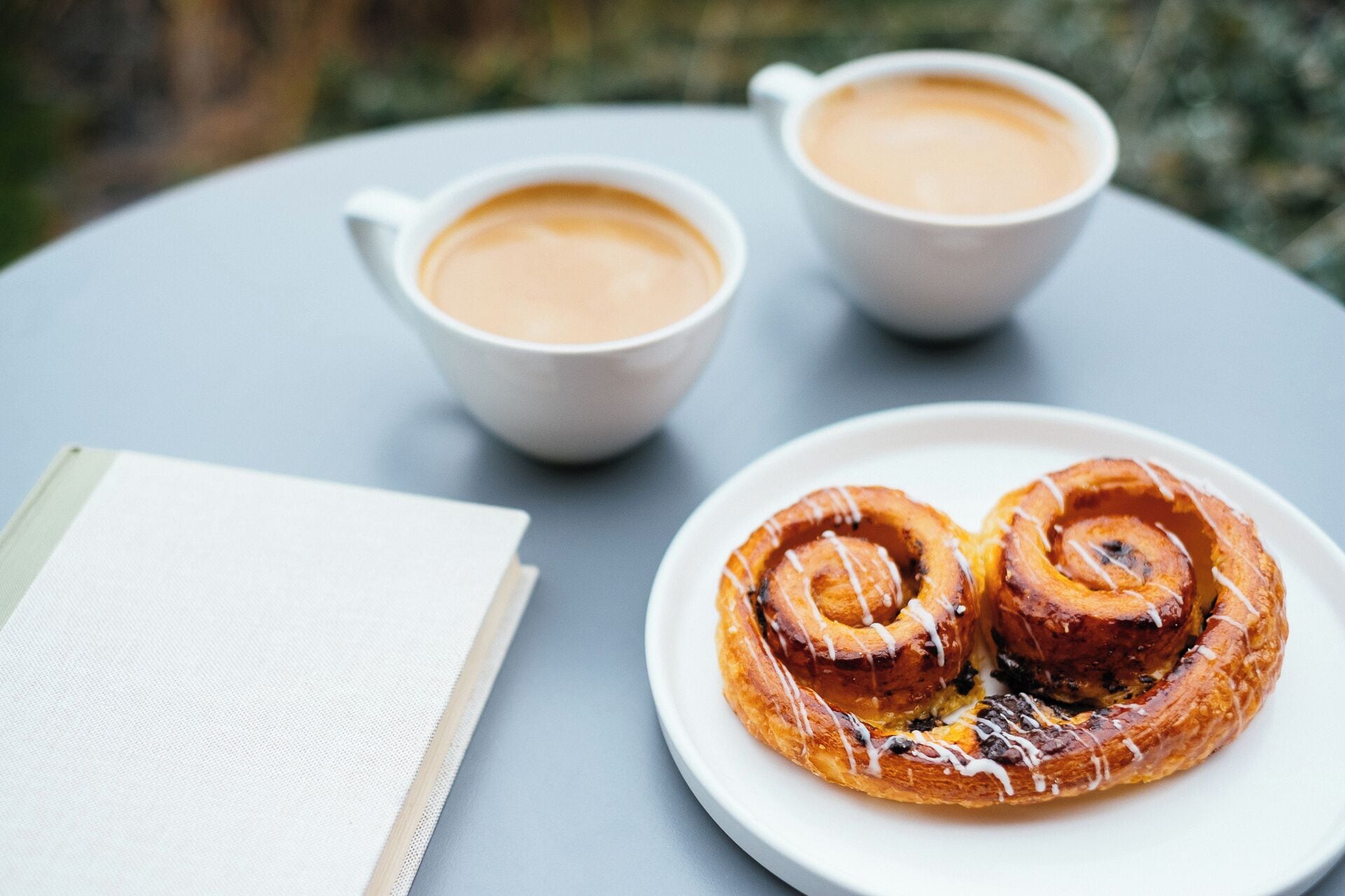 A table with two cups of coffee and a plate with two cinnamon rolls.