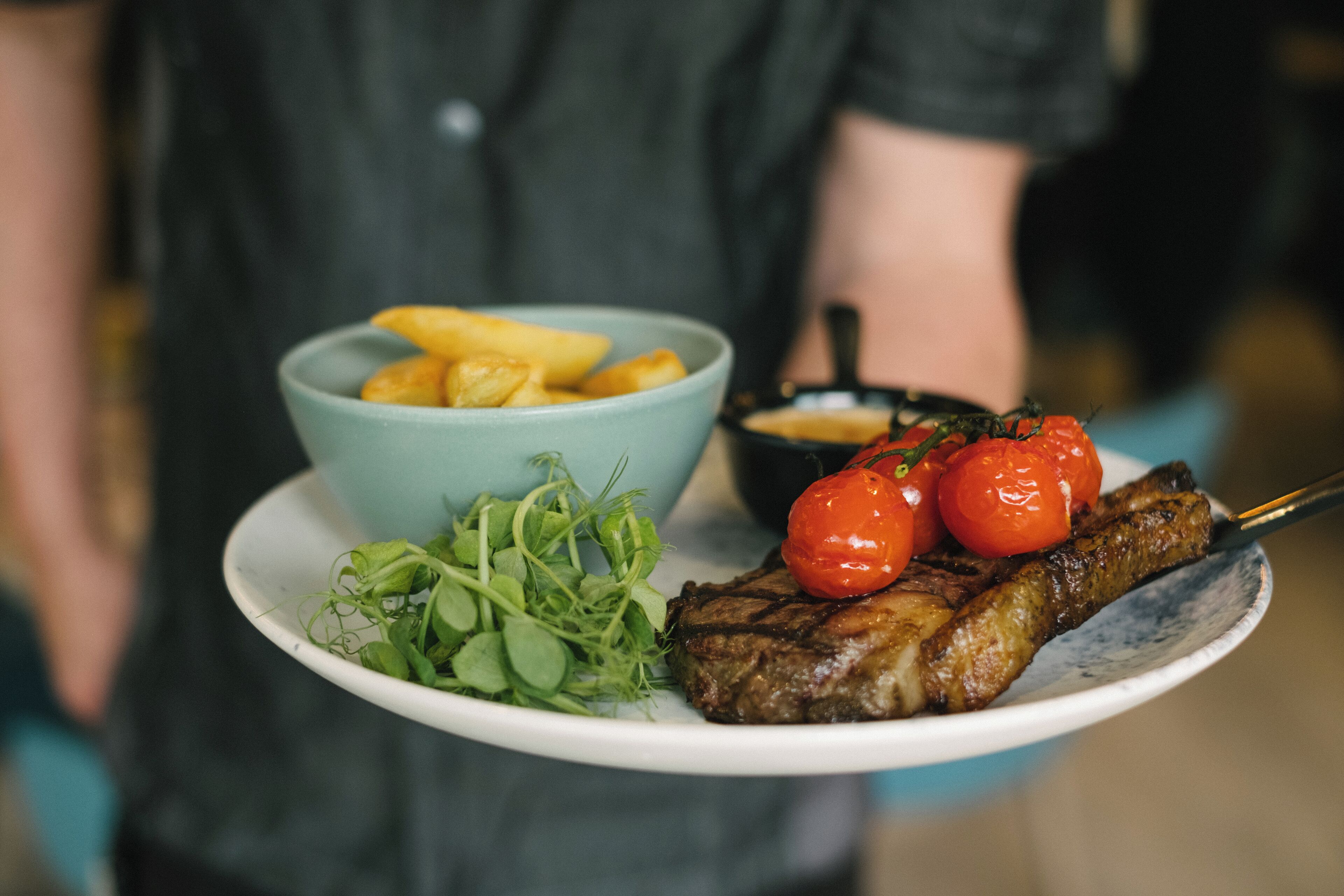 A plate with a grilled steak, cherry tomatoes, greens, and fries.