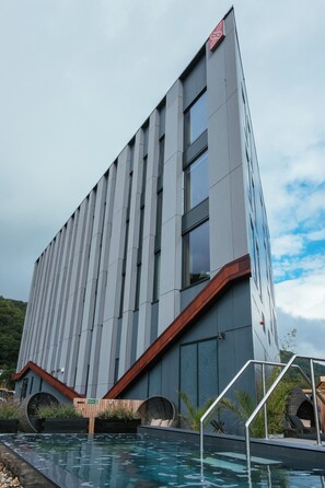 A modern building with a pool area, featuring a large window, a wooden deck, and a metal railing.