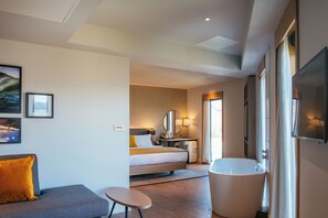 A modern hotel room with a bed, a sitting area, a bathroom, and a large window.