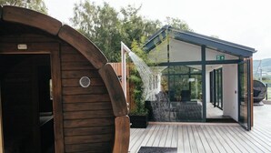 A wooden sauna structure with a glass-enclosed room and a water feature.