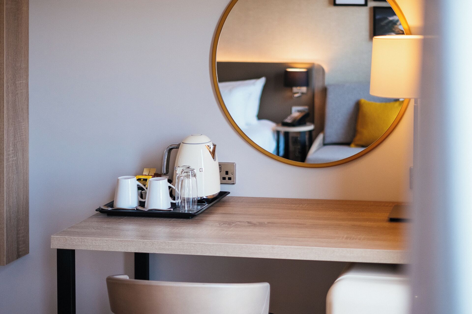 A hotel room with a wooden table, a coffee maker, and a tray with cups and a glass.