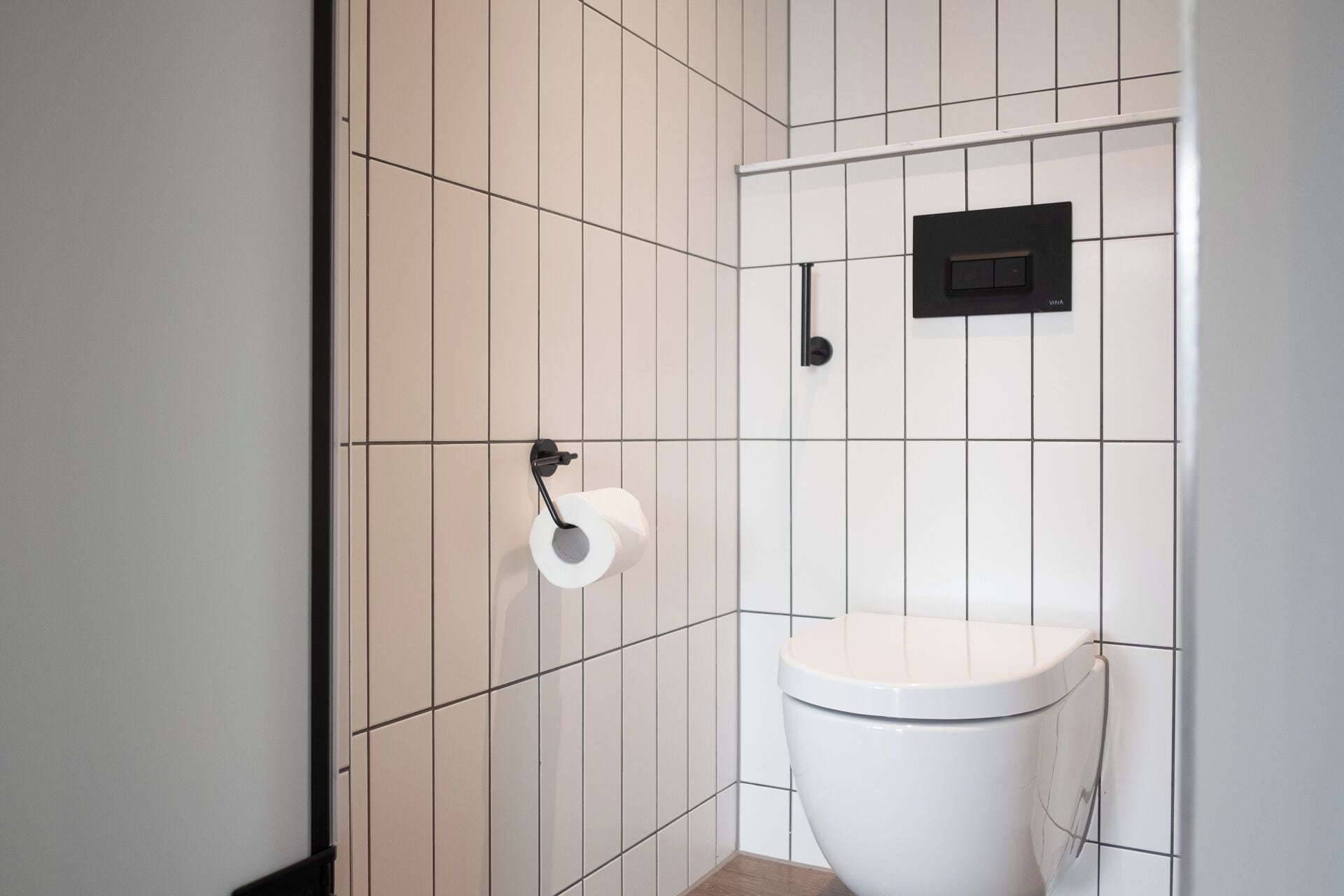 A small, modern bathroom with a toilet, a toilet paper holder, and a black electrical outlet on the wall.