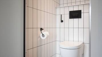 Un baño pequeño y moderno con inodoro, dispensador de papel higiénico y un enchufe eléctrico negro en la pared.