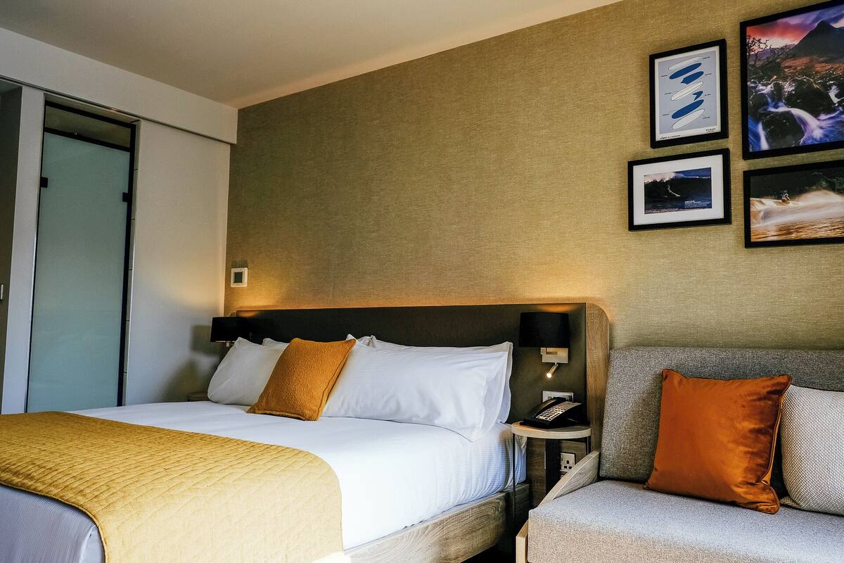 A hotel room with a bed, a bedside table with a phone, and a couch.