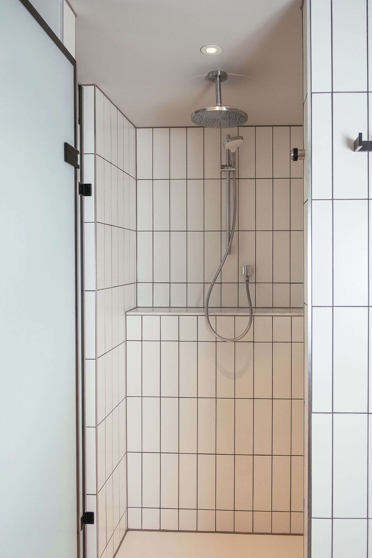 Ducha con cabezal de ducha manual y grifo empotrado, con azulejos en una tonalidad clara.