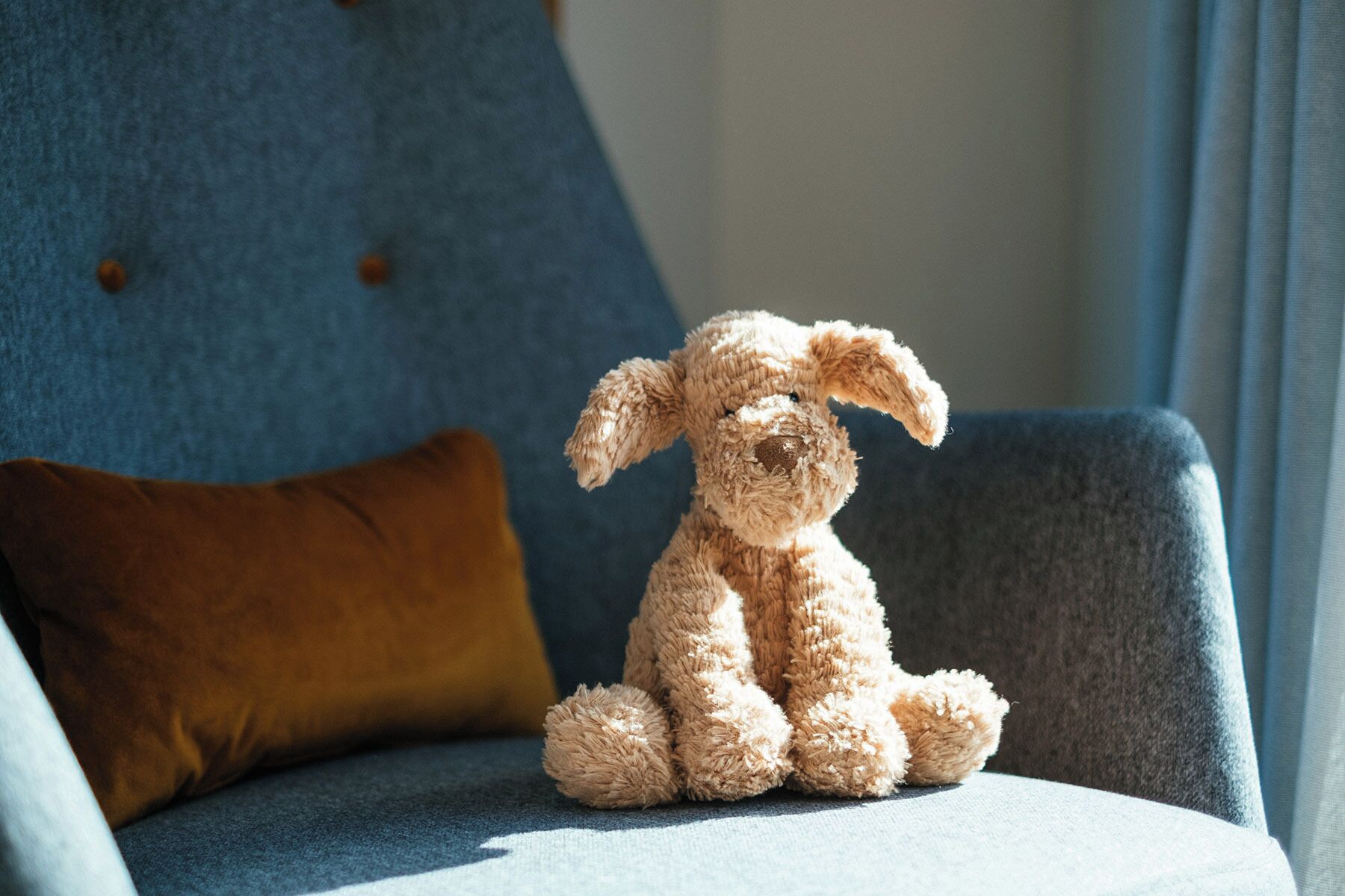 A plush toy on a chair with a brown cushion.