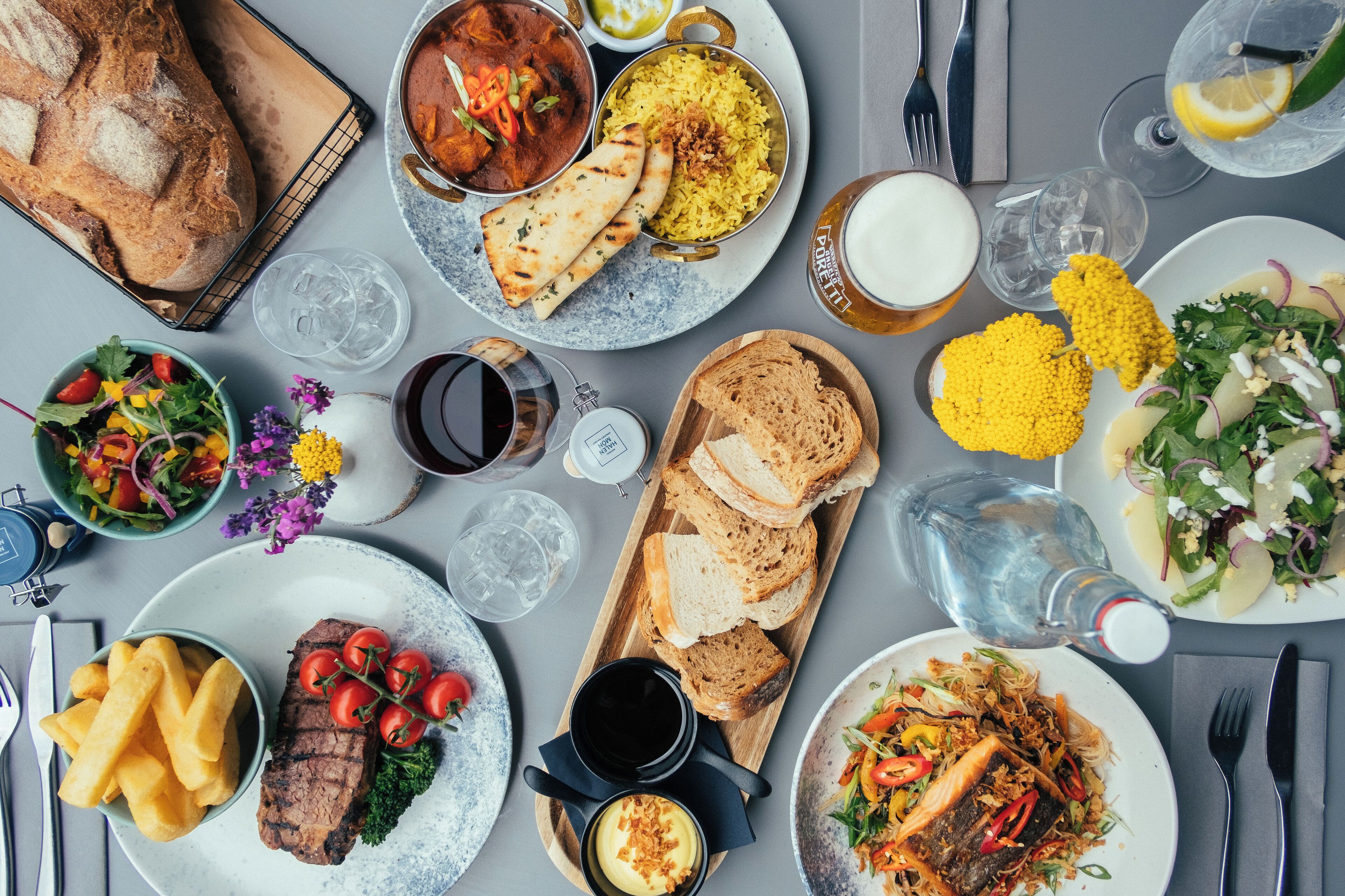 A table set with various dishes including bread, rice, salad, and meat, along with drinks and utensils.