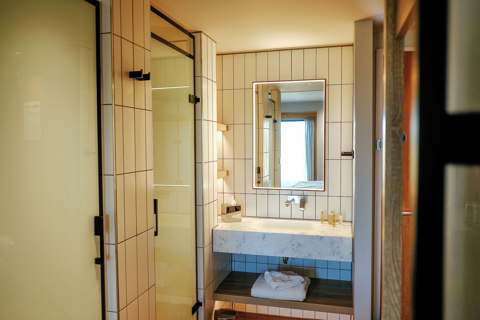 Ein Badezimmer mit einer Duschkabine aus Glas, einem Waschbecken mit Spiegel und einem Handtuch auf der Ablagefläche.