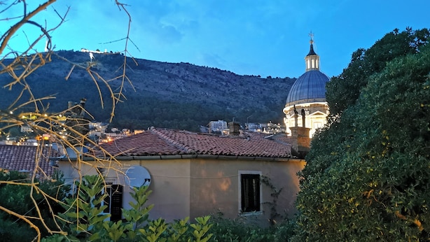 A building with a dome and a bell tower, surrounded by greenery and a mountainous backdrop. - Apartment Mama H (Dubrovnik)