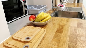A kitchen with a microwave, a bowl of fruit, a cutting board, and a sink. - Apartment Mama H (Dubrovnik)