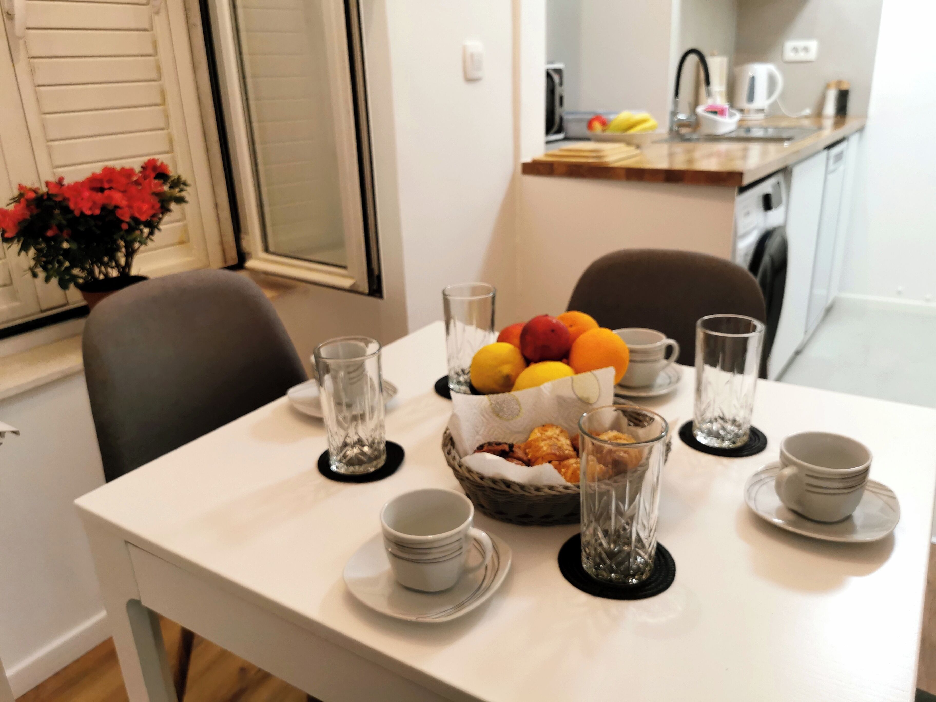 A dining table set with plates, bowls, glasses, and a fruit basket.