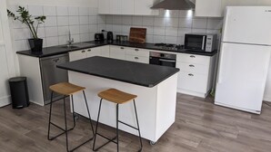 Eine moderne Küche mit weißen Schränken, einer schwarzen Arbeitsplatte, einer Edelstahl-Dunstabzugshaube, einer Mikrowelle, einem Kühlschrank und einer kleinen Kochinsel mit Hockern.