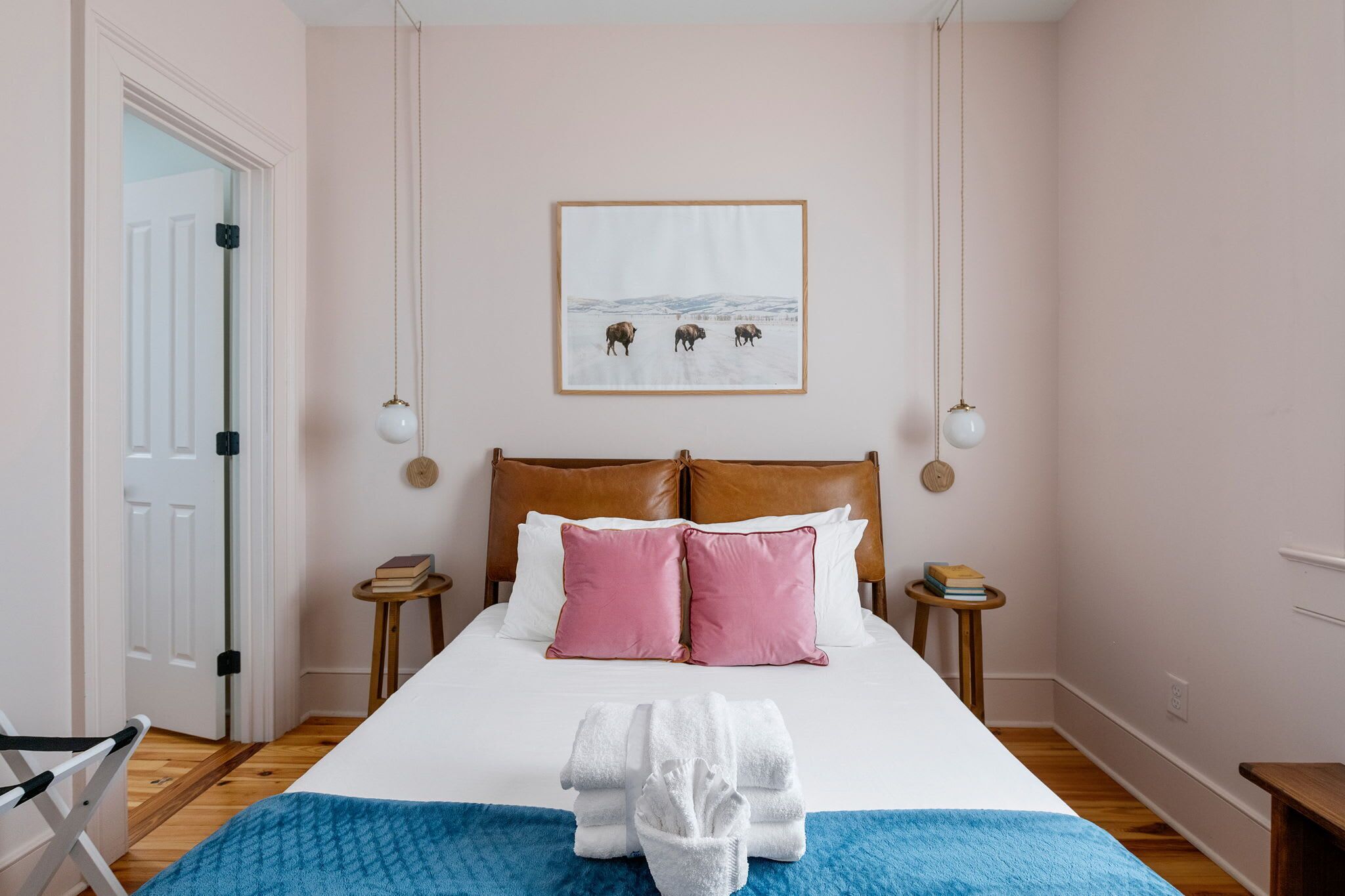 Une chambre à coucher bien rangée, avec un lit, des oreillers, une table de chevet et un tableau accroché au mur.
