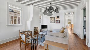 A spacious living room with a wooden floor, a sofa, a dining table with chairs, a TV, and a fireplace. - Oak Loft Downtown, Steps to King St Bars & Restaurants (Charleston)
