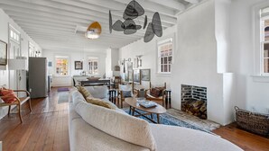 A spacious living room with a large sofa, a dining table, and a fireplace. There is a kitchen in the background with a refrigerator and a stove. - Oak Loft Downtown, Steps to King St Bars & Restaurants (Charleston)