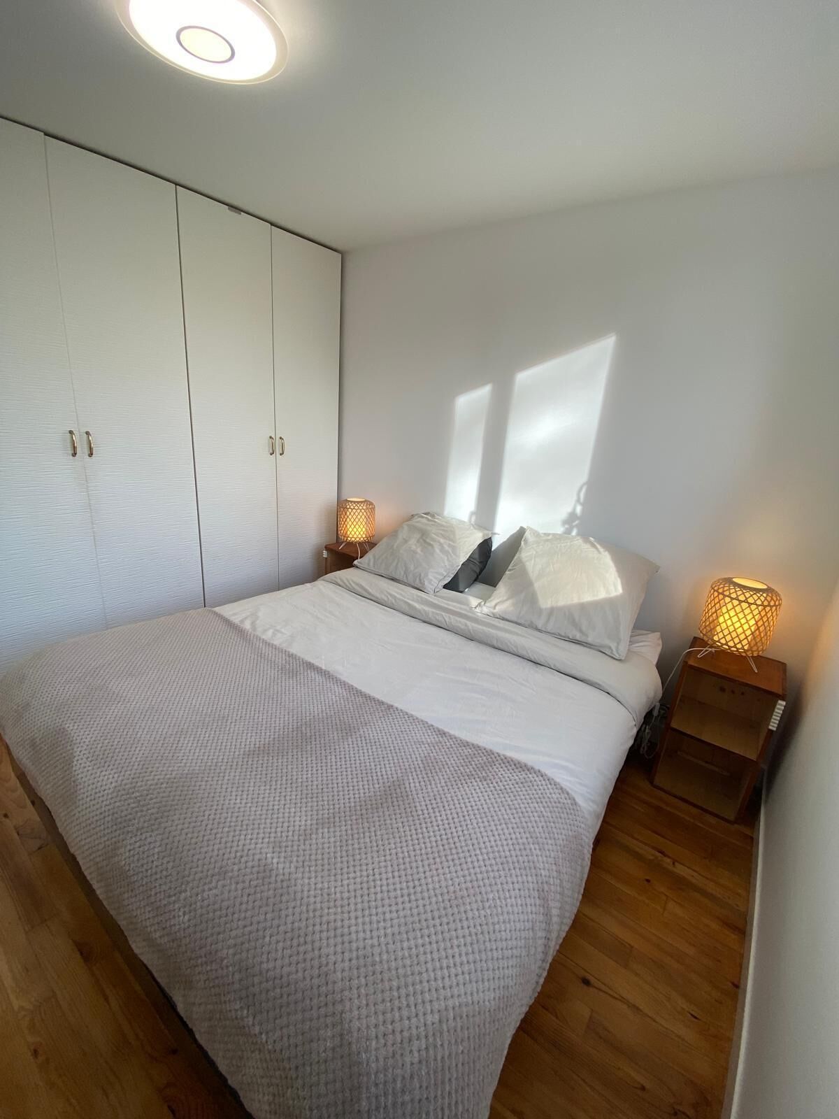 A bedroom with a large bed, white wardrobe, and two bedside lamps.
