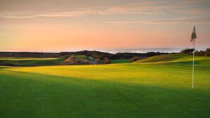 A golf course with a flagstick, rolling hills, and a sunset in the background.