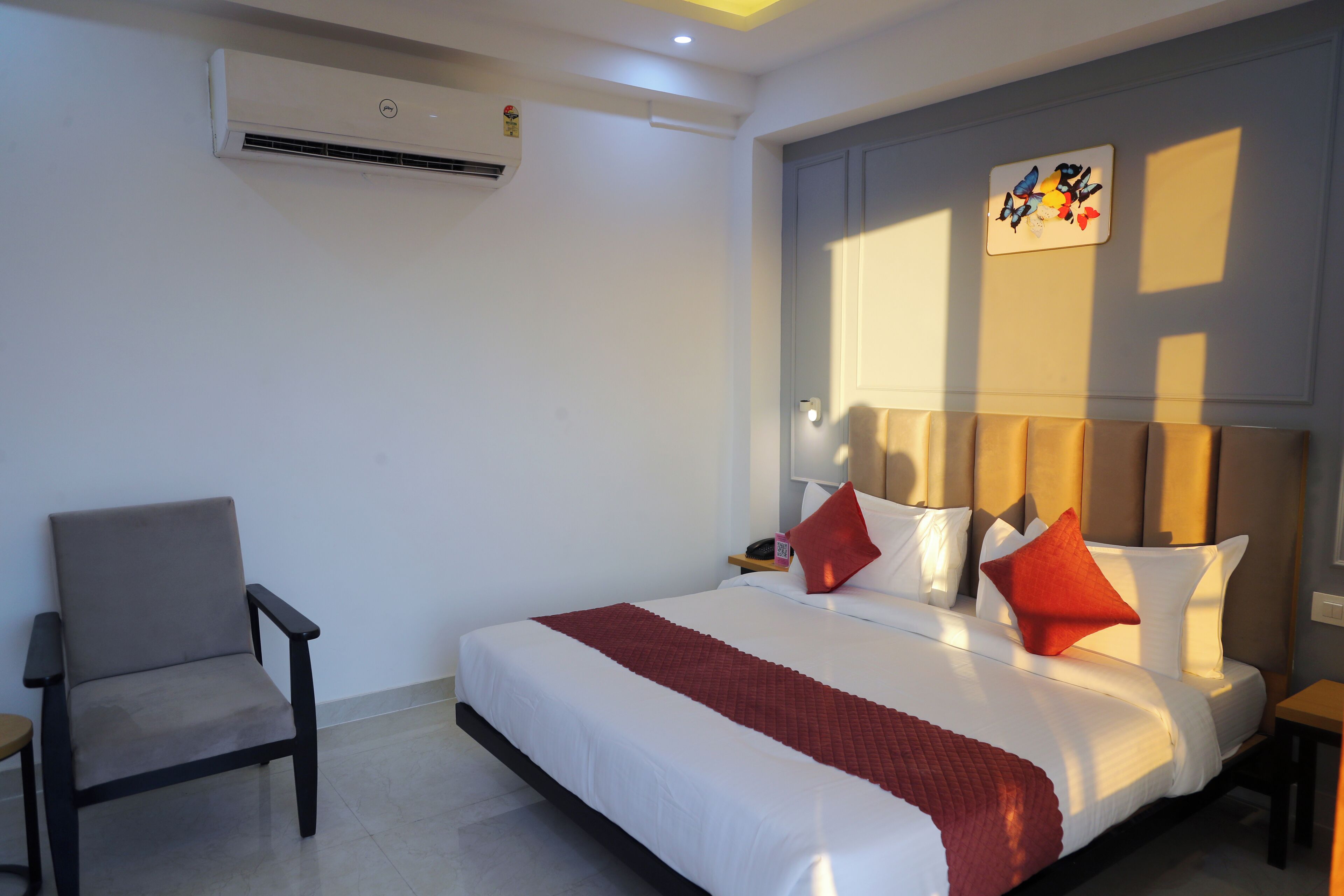 Quarto de hotel com uma cama grande, uma cadeira, uma mesinha de cabeceira e um ar condicionado.
