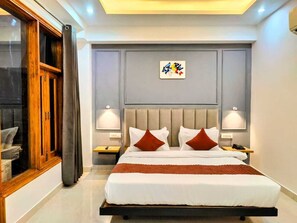 A modern hotel room with a large bed, two bedside tables, a nightstand, and a window with curtains. - Hotel Mavens House (Gurugram)