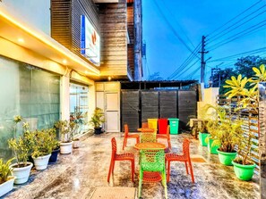 An outdoor seating area with tables and chairs, surrounded by potted plants. - Hotel Mavens House (Gurugram)