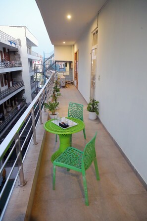 A balcony with a table and chairs, potted plants, and a railing. - Hotel Mavens House (Gurugram)