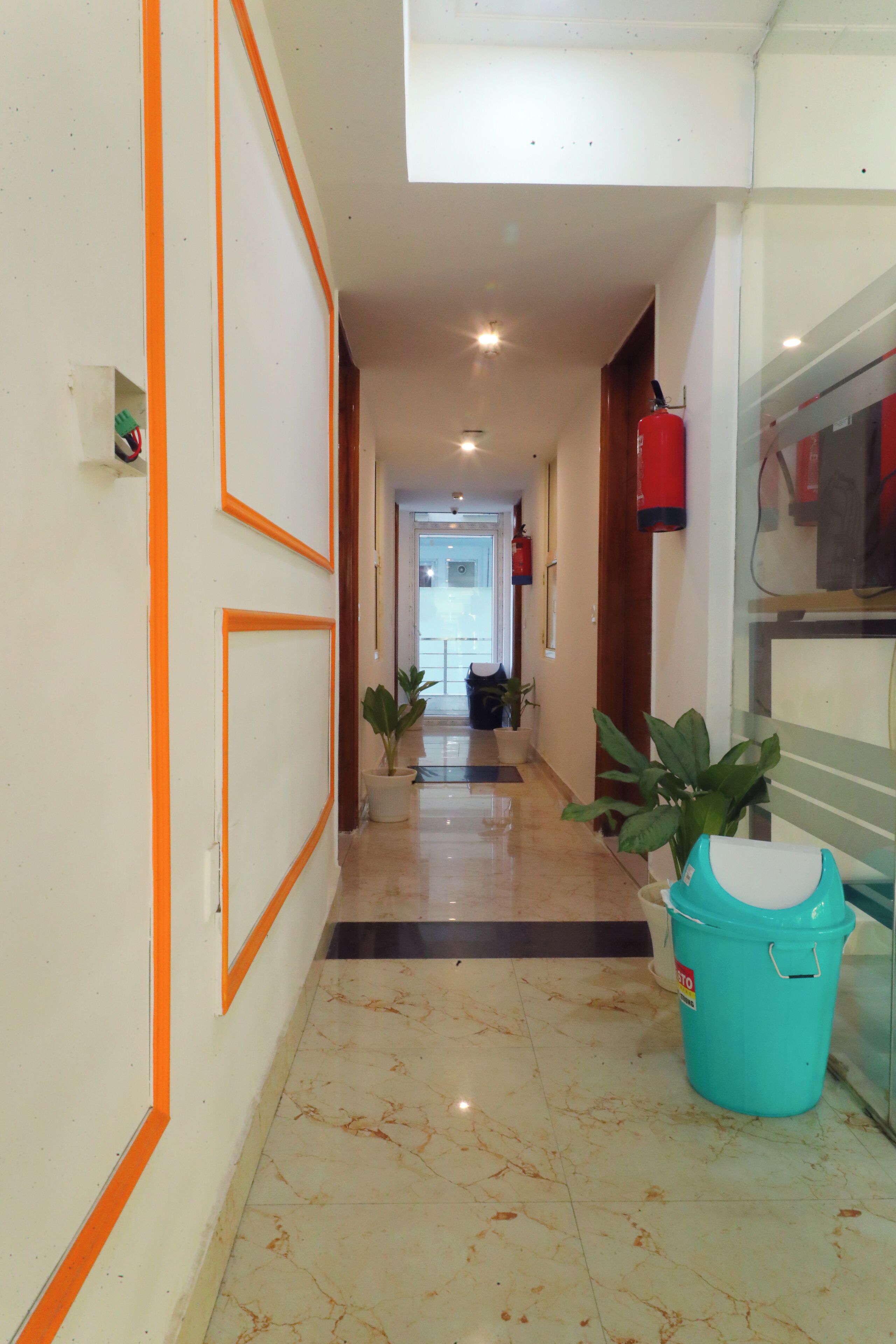 Un pasillo con suelo de baldosas, detalles naranja en las paredes y plantas en macetas.