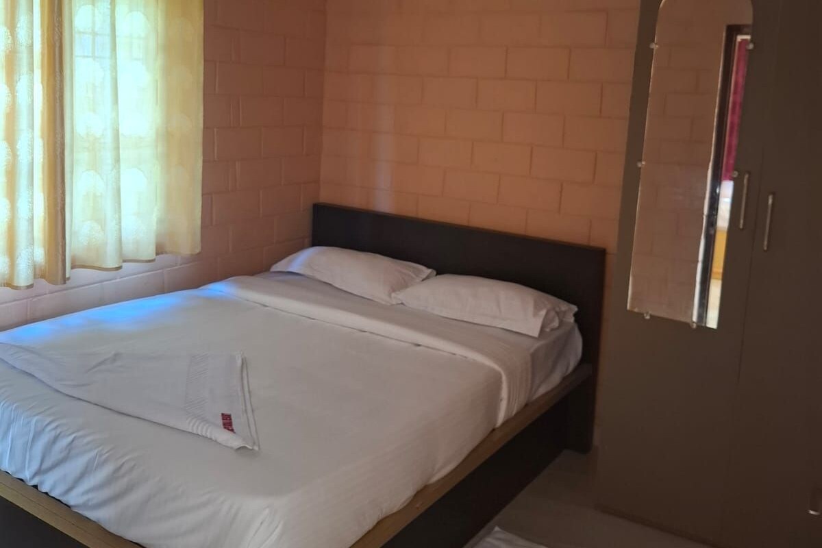 A bedroom with a bed, a ceiling fan, an air conditioning unit, a window with curtains, and a door with a mirror.