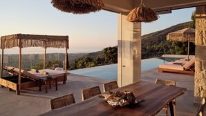 A luxurious outdoor seating area with a wooden table, wicker chairs, and a thatched canopy.