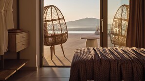 A bedroom with a bed, a wooden nightstand, a chair, and a view of the sea through a glass door.
