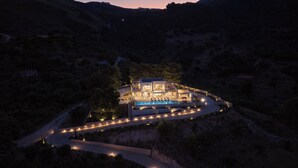 A large, modern house with a swimming pool, surrounded by a well-lit driveway and pathways.