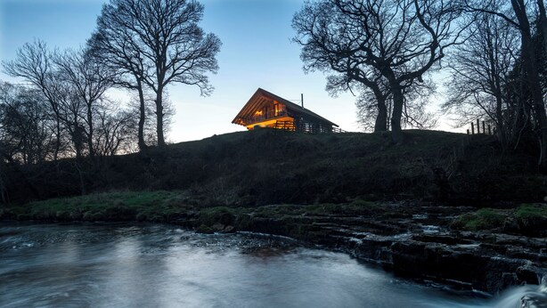 A cabin with a sloped roof, situated on a hill overlooking a river. - Luxury Secluded Log Cabin with a Hot Tub - Sleeps 8 - Dog Friendly - River View (Longtown)
