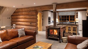 A log cabin interior with a central fireplace, wooden walls, a dining area, and a kitchen. - Luxury Secluded Log Cabin with a Hot Tub - Sleeps 8 - Dog Friendly - River View (Longtown)