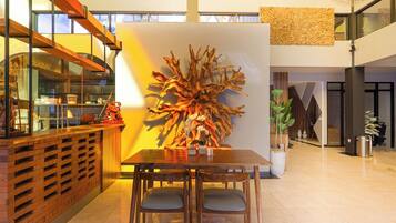 Un intérieur moderne avec un comptoir d’accueil en bois, une grande œuvre d’art abstraite murale et un espace repas comprenant une table et des chaises.