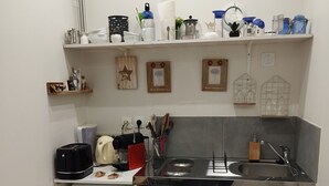 Une cuisine compacte équipée d’un four à micro-ondes, d’un grille-pain et d’un évier. On y trouve des étagères contenant divers ustensiles de cuisine et une petite poubelle.