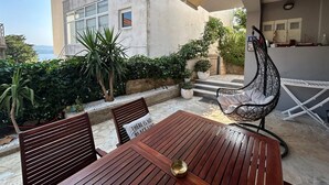 Un patio al aire libre con una mesa y sillas de madera, una silla colgante y macetas con plantas.