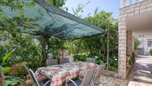 Eine Terrassengruppe mit Tisch und Stühlen, überdacht von einer Glaskonstruktion, umgeben von Grünpflanzen und Steinmauern.
