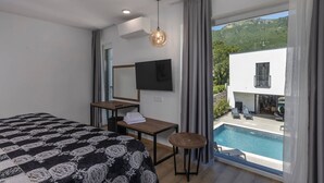 A modern hotel room with a bed, a desk, a TV, and a view of a pool and hillside. - NEW! Villa with 6 Bedrooms and Heated Pool (Moscenicka Draga)