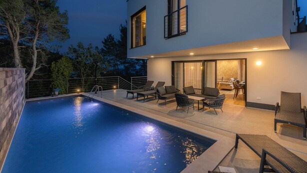 Ett modernt hus i två våningar med en swimmingpool, en uteplats och en matplats.