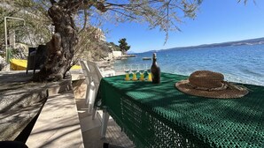 Une table dressée avec une bouteille et des verres, donnant sur une vue côtière sous un ciel dégagé.
