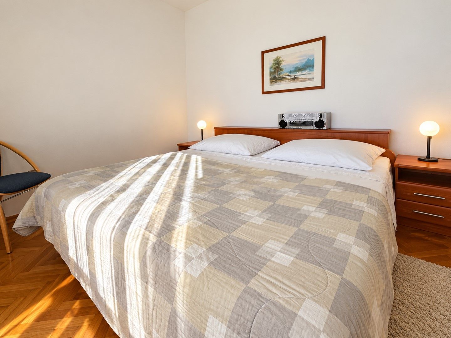 A bedroom with a bed, bedside tables, a chair, a painting on the wall, and a lamp.