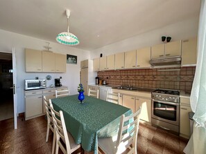 Een kleine keuken met een eettafel, stoelen, een magnetron, een fornuis en kastjes.
