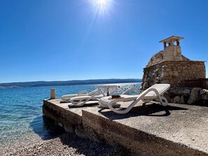 A stone structure with a small pavilion, white lounge chairs, and a clear view of the sea. - Azure Apartments By The Sea with 3 Bedrooms (Omis)