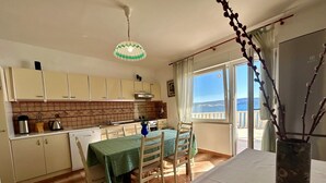 A compact kitchen with a dining area, a view of the sea, and a balcony with a railing. - Azure Apartments By The Sea with 3 Bedrooms (Omis)