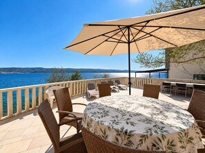A terrace with wicker furniture, a table with a leaf-patterned tablecloth, and a large umbrella providing shade.