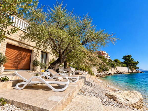 A seaside hotel with outdoor seating, a clear view of the sea, and a building with a large garage door.